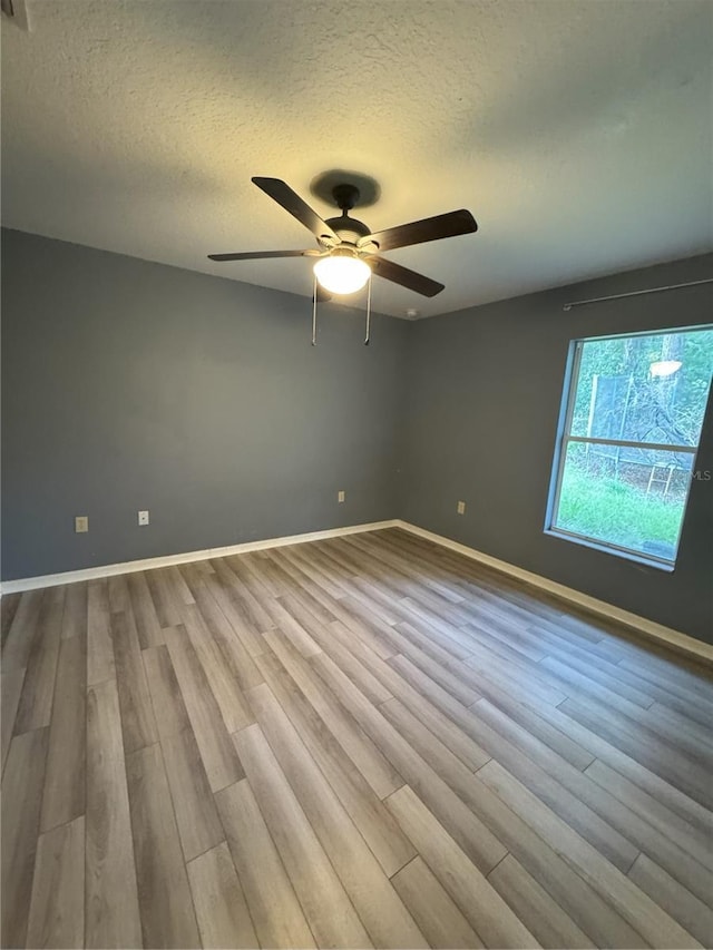 unfurnished room featuring baseboards, a ceiling fan, wood finished floors, and a textured ceiling