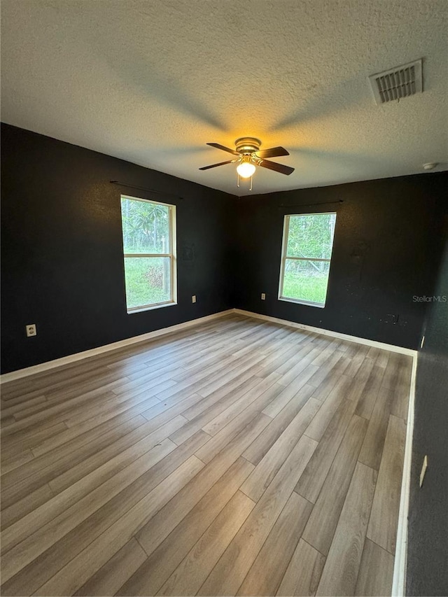 spare room with wood finished floors, a textured ceiling, ceiling fan, baseboards, and visible vents