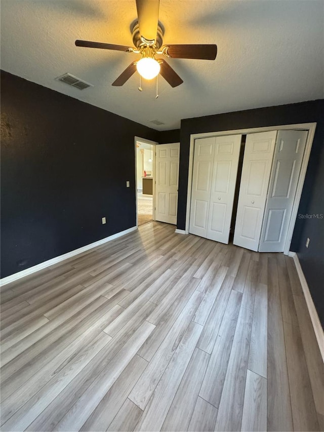 unfurnished bedroom featuring ceiling fan, a closet, light hardwood / wood-style floors, and a textured ceiling