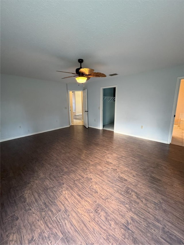 empty room with a textured ceiling, ceiling fan, visible vents, baseboards, and dark wood-style floors