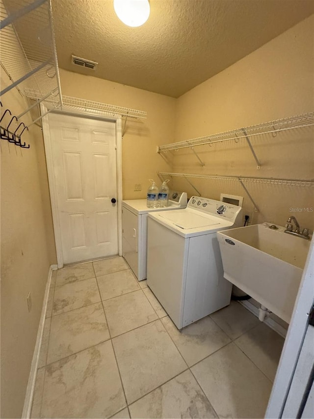 washroom with a textured ceiling, washer and clothes dryer, a sink, visible vents, and laundry area