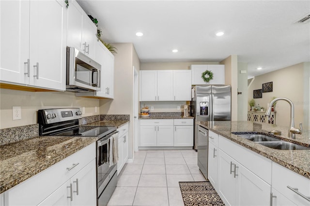 kitchen featuring appliances with stainless steel finishes, light tile patterned floors, sink, white cabinetry, and stone countertops