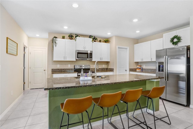 kitchen featuring a center island with sink, white cabinetry, a kitchen bar, and appliances with stainless steel finishes