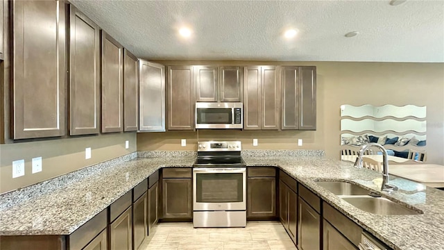 kitchen with light stone countertops, appliances with stainless steel finishes, sink, and a textured ceiling