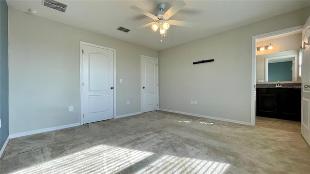 unfurnished bedroom with sink, light colored carpet, ensuite bathroom, and ceiling fan