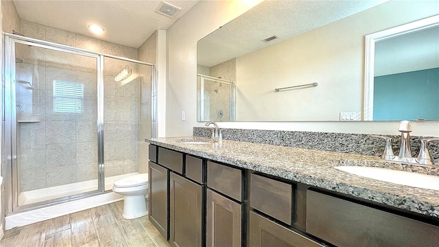 bathroom featuring vanity, toilet, a textured ceiling, a shower with shower door, and hardwood / wood-style floors