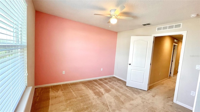 unfurnished bedroom with ceiling fan, light colored carpet, and a textured ceiling