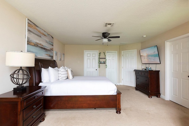 bedroom featuring light colored carpet, multiple closets, a textured ceiling, and ceiling fan