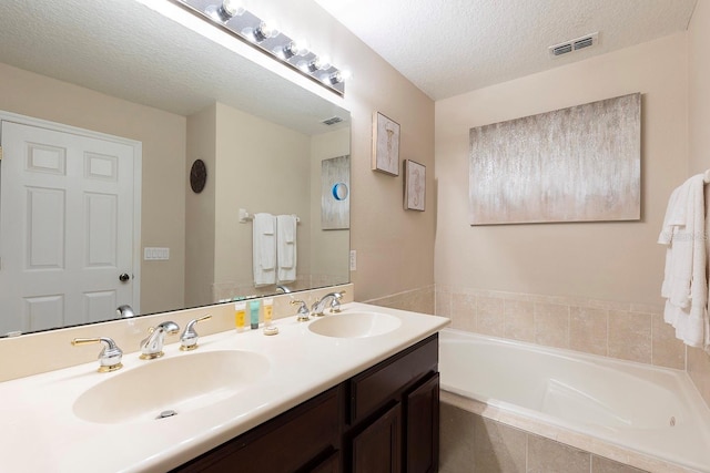 bathroom with vanity, tiled bath, and a textured ceiling