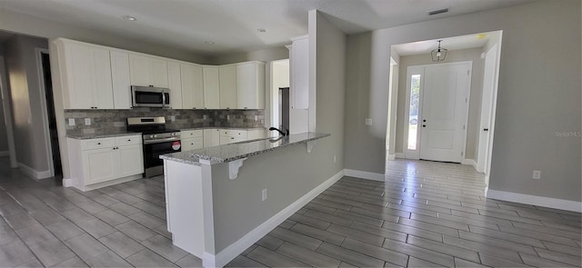 kitchen with tasteful backsplash, visible vents, light stone countertops, a peninsula, and stainless steel appliances