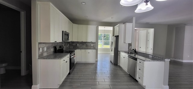 kitchen with light stone counters, decorative backsplash, a peninsula, stainless steel appliances, and a sink