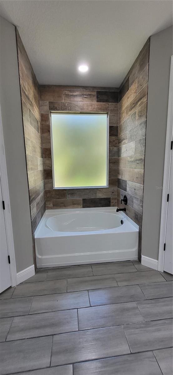 bathroom featuring a bath, a healthy amount of sunlight, and baseboards