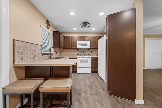 kitchen with white appliances, sink, kitchen peninsula, a breakfast bar area, and light hardwood / wood-style flooring