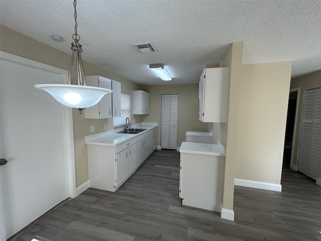 kitchen featuring dark wood-type flooring, sink, pendant lighting, white cabinets, and a textured ceiling