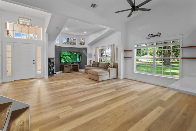 living room with hardwood / wood-style flooring, a towering ceiling, and ceiling fan with notable chandelier