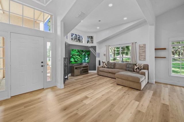 entryway featuring beam ceiling, a towering ceiling, and light wood-type flooring