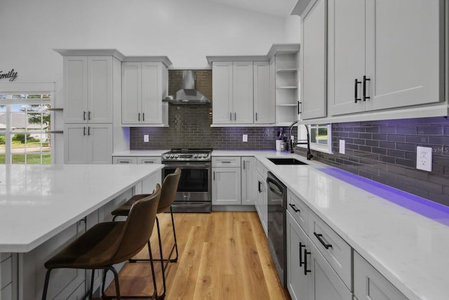 kitchen with sink, a breakfast bar area, dishwasher, stainless steel stove, and wall chimney range hood