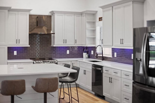 kitchen with sink, appliances with stainless steel finishes, a kitchen breakfast bar, wall chimney range hood, and white cabinets