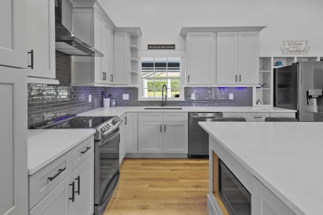 kitchen featuring wall chimney exhaust hood, sink, white cabinetry, light hardwood / wood-style flooring, and appliances with stainless steel finishes