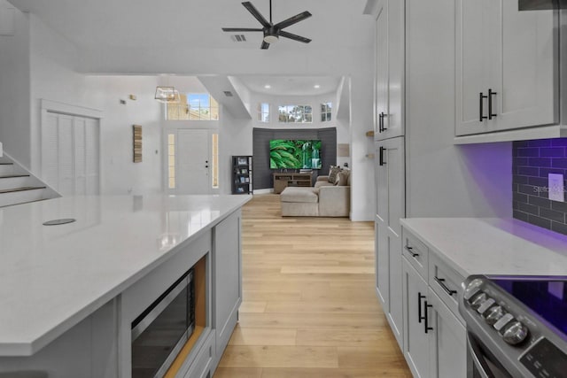 kitchen with ceiling fan, appliances with stainless steel finishes, light stone counters, decorative backsplash, and light wood-type flooring