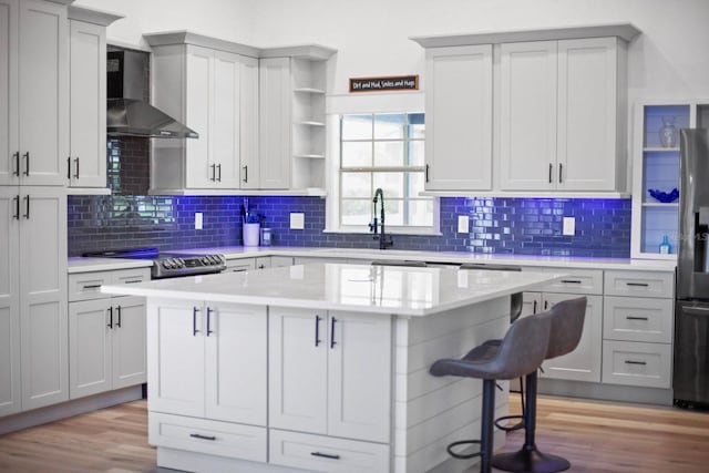 kitchen featuring wall chimney range hood, light hardwood / wood-style floors, a breakfast bar, and a kitchen island