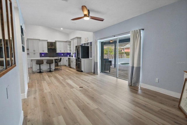 kitchen featuring stainless steel appliances, a kitchen bar, vaulted ceiling, and light hardwood / wood-style flooring