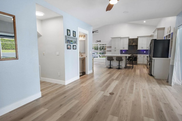 kitchen featuring wall chimney exhaust hood, appliances with stainless steel finishes, a kitchen breakfast bar, a kitchen island, and a healthy amount of sunlight