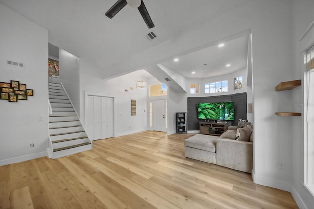 living room featuring a towering ceiling, ceiling fan, and light wood-type flooring