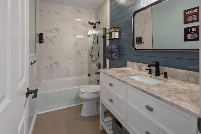 full bathroom with toilet, tiled shower / bath, vanity, wooden walls, and tile patterned flooring