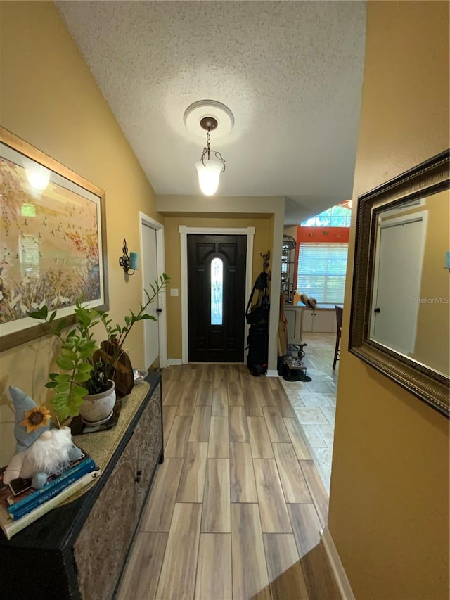 foyer with light hardwood / wood-style floors, a textured ceiling, and vaulted ceiling