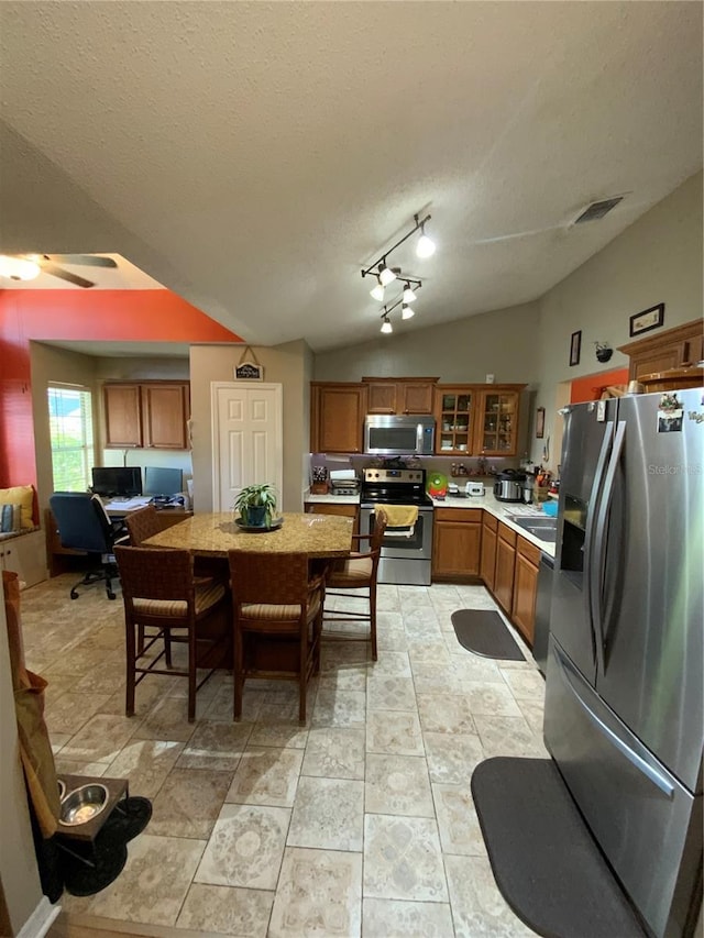 2939 Falling Tree Cir, Orlando, FL 32837 - kitchen with appliances with stainless steel finishes, brown cabinetry, light countertops, a textured ceiling, and vaulted ceiling