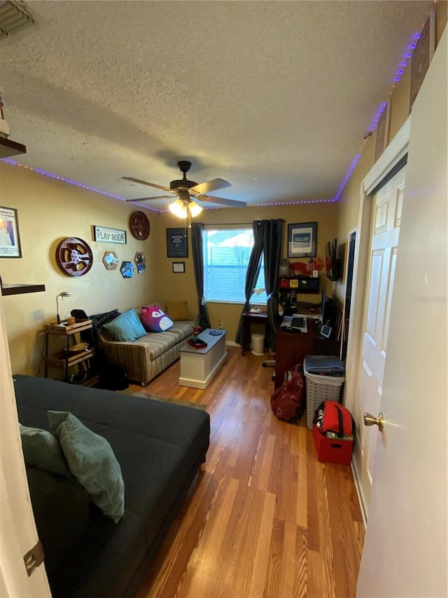 living room featuring a textured ceiling, wood-type flooring, and ceiling fan