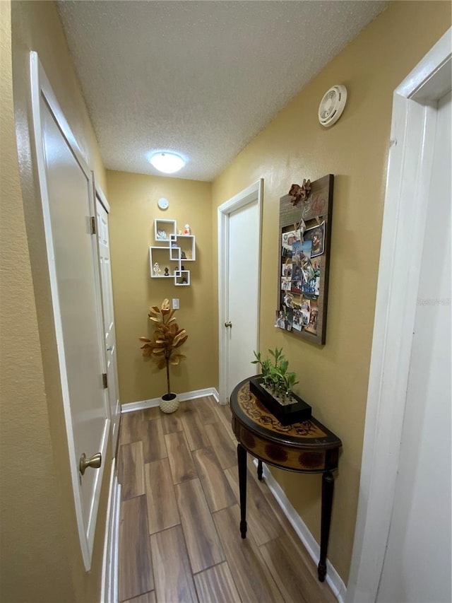 hall with a textured ceiling and wood-type flooring