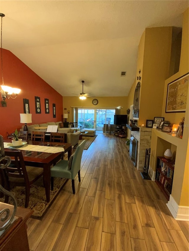 dining area featuring hardwood / wood-style floors, ceiling fan with notable chandelier, and vaulted ceiling