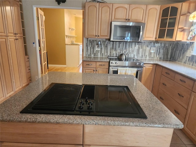 kitchen featuring light brown cabinetry, backsplash, stainless steel appliances, light stone counters, and light hardwood / wood-style flooring