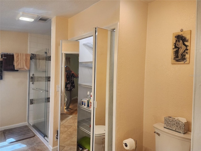 bathroom with a shower with door, toilet, a textured ceiling, and tile patterned flooring