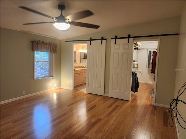 unfurnished bedroom with a barn door, light wood-type flooring, a closet, and ceiling fan