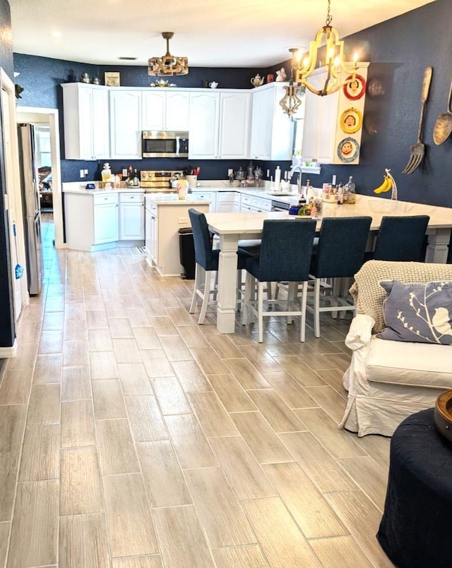 kitchen featuring white cabinetry, appliances with stainless steel finishes, decorative light fixtures, sink, and a breakfast bar area