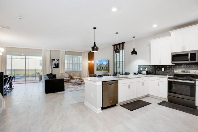 kitchen featuring white cabinets, kitchen peninsula, tasteful backsplash, decorative light fixtures, and appliances with stainless steel finishes