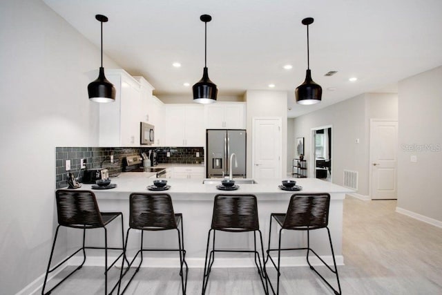 kitchen featuring light wood-type flooring, tasteful backsplash, kitchen peninsula, white cabinets, and appliances with stainless steel finishes