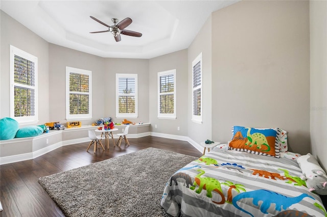 bedroom with dark wood-type flooring, a raised ceiling, and ceiling fan