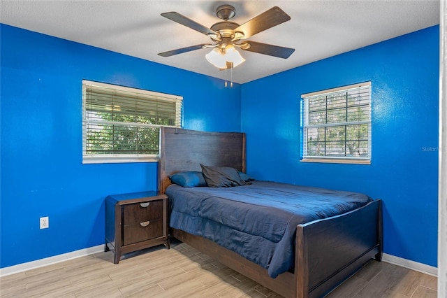 bedroom featuring ceiling fan, a textured ceiling, multiple windows, and light wood-type flooring