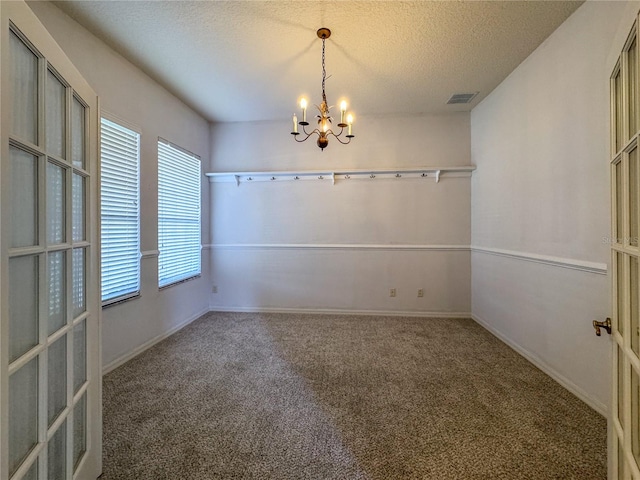 spare room featuring a textured ceiling, carpet floors, and an inviting chandelier