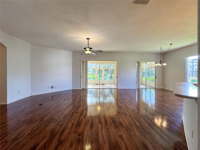 unfurnished living room featuring dark wood-type flooring, a textured ceiling, and ceiling fan with notable chandelier