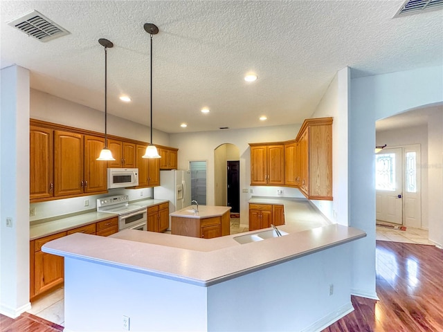 kitchen featuring white appliances, light wood-type flooring, a textured ceiling, a center island, and pendant lighting