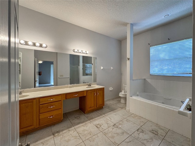 bathroom featuring vanity, a textured ceiling, toilet, and tiled bath