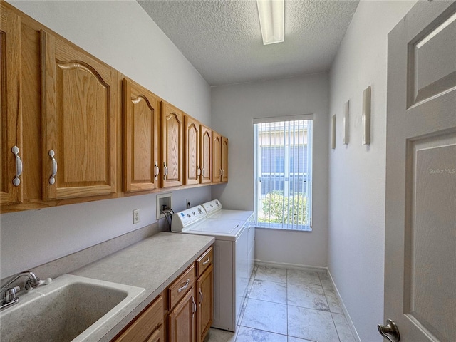 laundry area featuring sink, light tile patterned flooring, cabinets, a textured ceiling, and washing machine and dryer