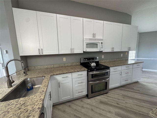 kitchen with light stone countertops, sink, range with two ovens, white cabinets, and light wood-type flooring