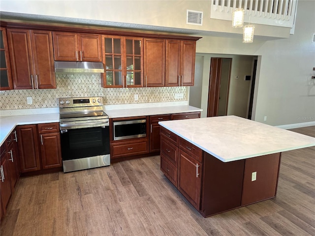 kitchen with appliances with stainless steel finishes, hanging light fixtures, dark wood-type flooring, and tasteful backsplash