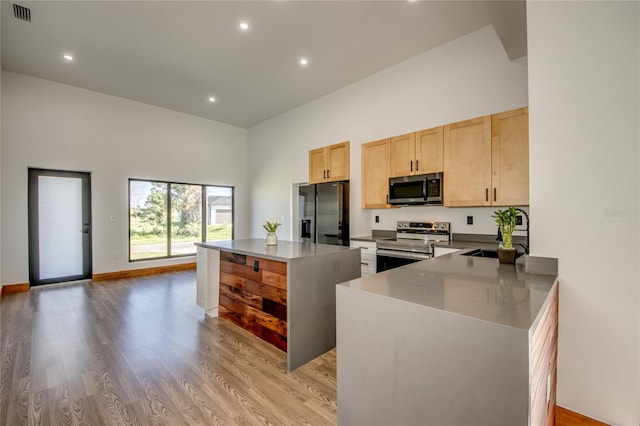 kitchen featuring kitchen peninsula, light wood-type flooring, stainless steel appliances, sink, and light brown cabinets